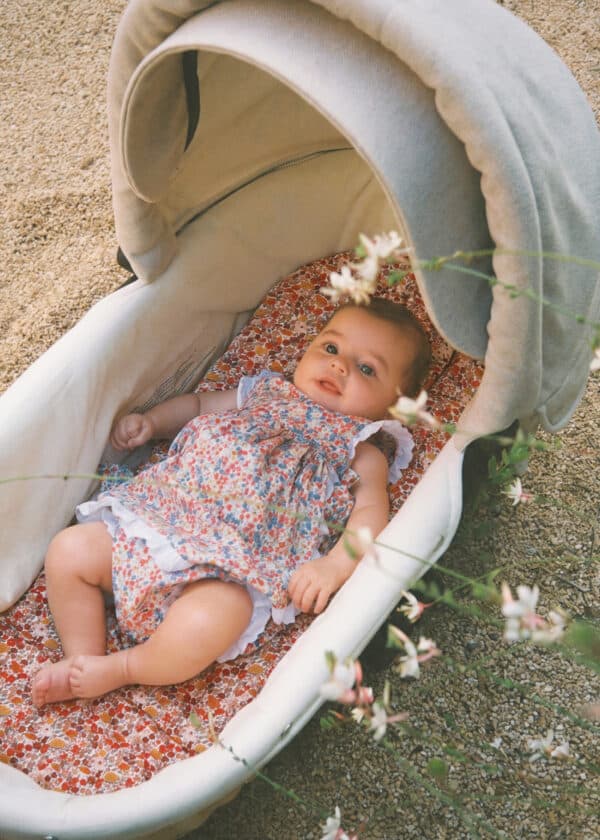 Baby lying in textile basket with ErgoTopper Claire, floral pattern in red and blue, cream-colored canopy