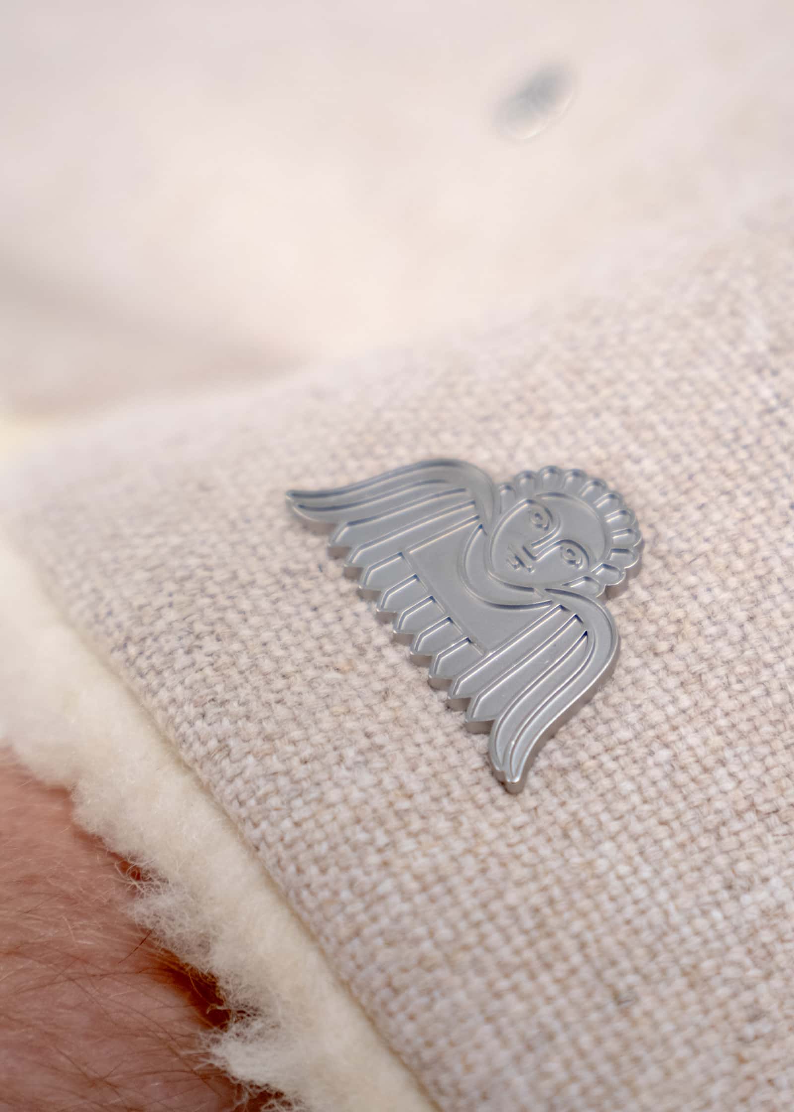 Silbernes ANGELCAB Engel-Emblem auf beigem Wollstoff des Handmuffs Upminster mit Lammfellfutter