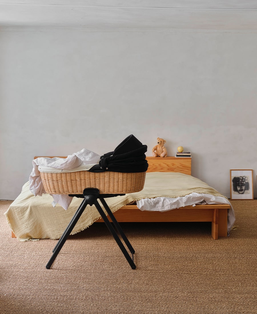 Korbwanne mit schwarzem Verdeck auf schwarzem Wiegengestell vor Holzbett im Schlafzimmer